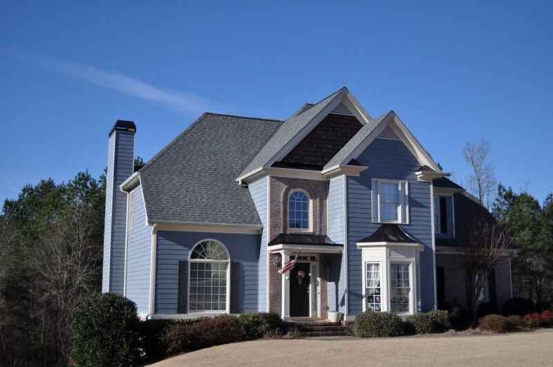 photo of blue hardi sided home with entry dormers and steep pitched roofline. The architectural dark slate roof sets off the blue of the exterior of the home.