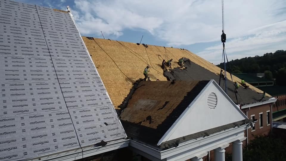 Aerial view of new roof underlay sections with one section of roof with team working to remove old roof materials