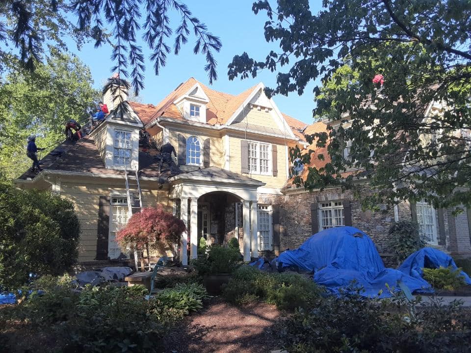 mature landscaping on the front of the home requires careful work to protect the plantings while the roof is being replaced.