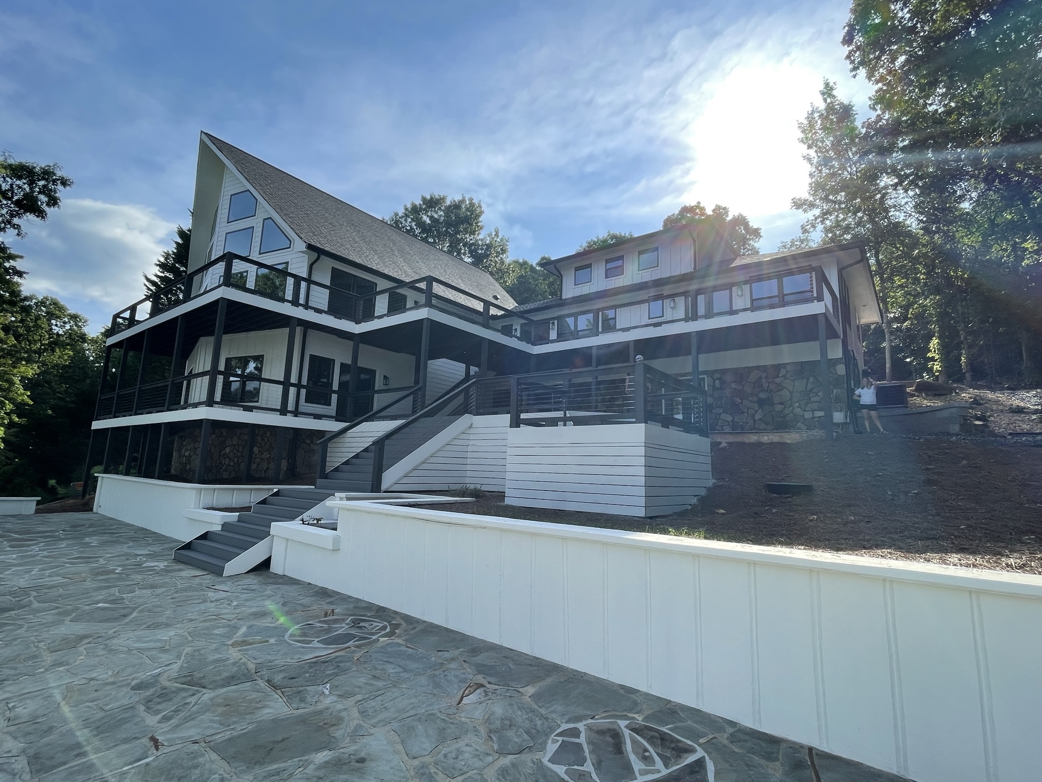 Photo of home from rear with rennovations completed showing new retaining walls framing and supporting the entire lower deck system and patio of the dock, Photo shows full upper level deck systems and rear facing windows