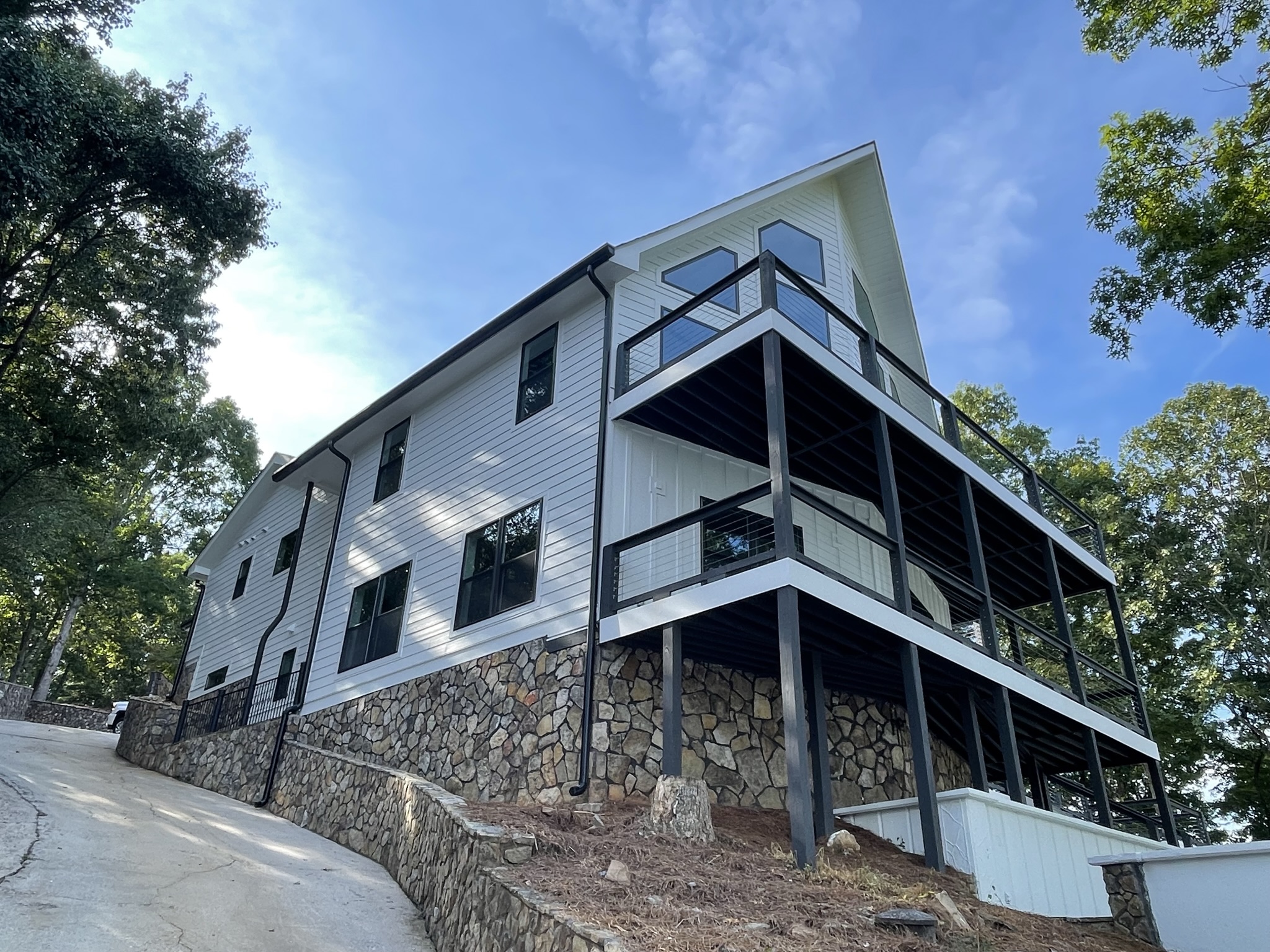 Photo from below the home on the lake side/rear side of home showing the corner of the home and paved drive system to the dock level