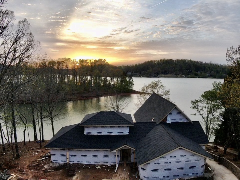 Photo at dusk of the newly roofed home and the lake with the sunset