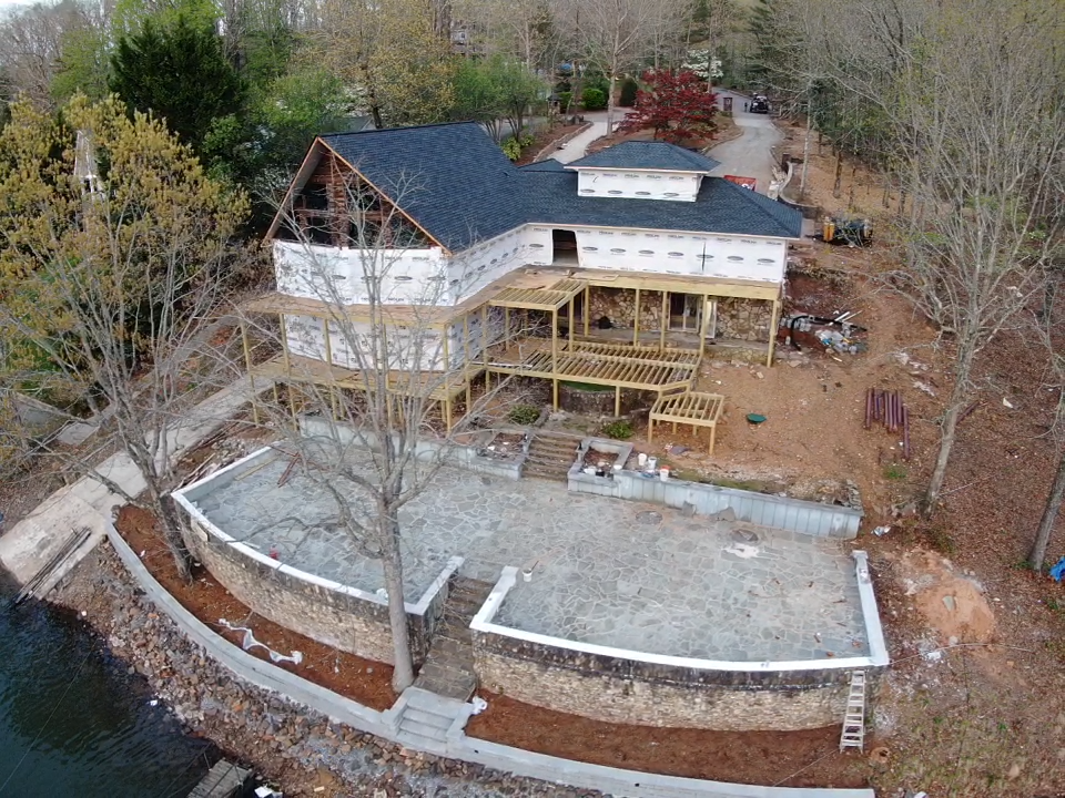 aeral photo of the rear of the home with extensive patio leading to the water and the decks under construction with the new roof having just een completed.