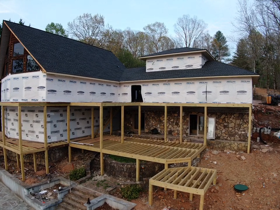 closer photo aerial view of the rear of the home iwth framed decks and wrapped house with new installed roof